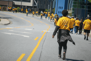 Protesters in yellow shirts walking on city street during demonstration, advocating for social chang.