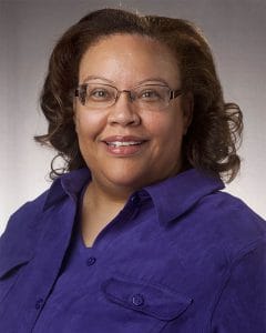 Professional woman with glasses in a purple shirt smiling for a headshot.