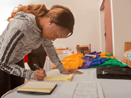 Woman organizing colorful T-shirts and supplies for event at CAES News.