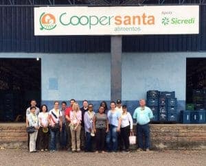 Group photo of Cooper Santa Alimentos team at CAES News facility with warehouse background.