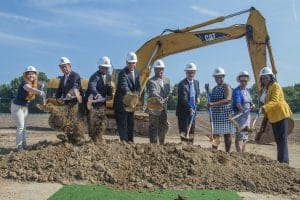 Group of professionals and officials at groundbreaking ceremony with excavator.