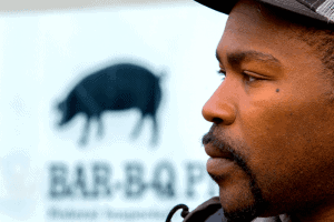 Close-up of a man with a barbecue restaurant sign in the background.
