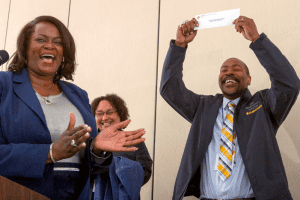 Group of professionals celebrating success at CAES News event, smiling and clapping.