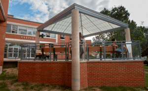 Outdoor pavilion with students, brick base, and metal railing at CAES News campus.