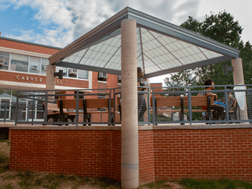 Outdoor pavilion with students, brick base, and metal railing at CAES News campus.