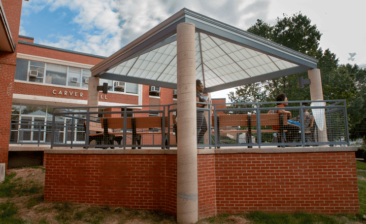 Outdoor pavilion with students, brick base, and metal railing at CAES News campus.