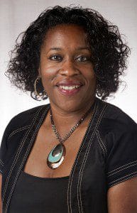 Portrait of a confident professional woman with curly hair, wearing a black blazer and statement nec.