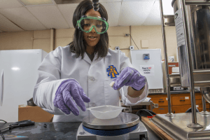 Scientist in laboratory wearing safety goggles and gloves, working with scientific equipment.