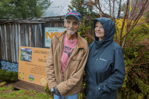 A lush outdoor scene with two people standing near a signboard in a garden or farm setting.