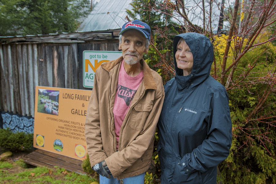 A lush outdoor scene with two people standing near a signboard in a garden or farm setting.