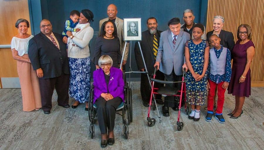 A woman in a wheelchair surrounded by diverse group of people at a memorial event.