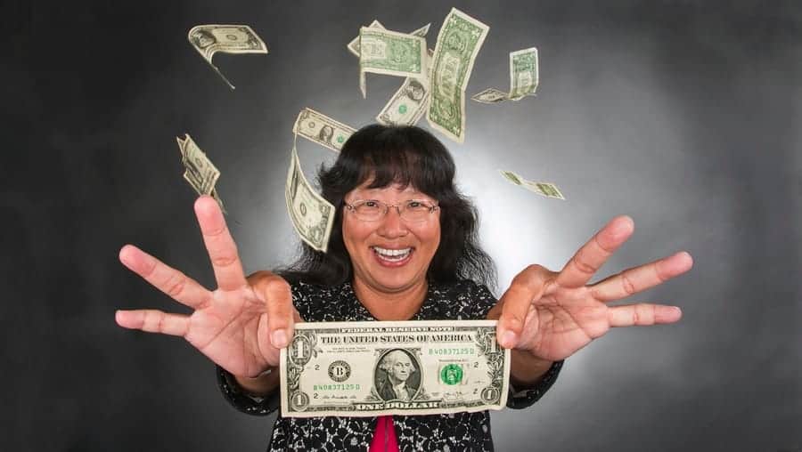 A woman smiling and holding a dollar bill with money flying around her.