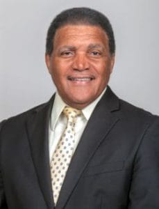 A man in a black suit and white shirt smiling for a professional portrait.