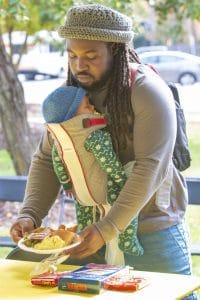 Father with child in baby carrier enjoying outdoor picnic in park.