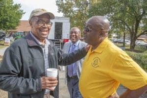 Enjoying a friendly outdoor conversation at a community event, with smiling men in casual and yellow.