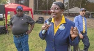 Empowered woman speaking at outdoor event with microphone and audience.