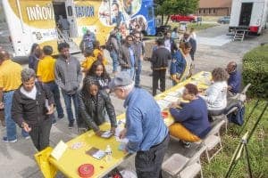 Accessible community event with people registering at a table outdoors, featuring a mobile informati.
