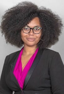 Diverse professional woman with natural curly hair wearing glasses and a black blazer with a pink bl.
