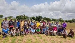 Community gathering of diverse people outdoors in a rural setting, participating in a group event.