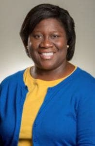 Empowered woman smiling, wearing a blue cardigan and yellow top, representing leadership and confide.