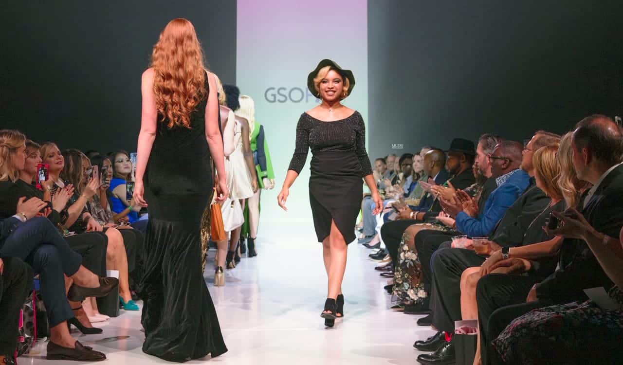 Elegant woman walking down the runway at a fashion show with an audience on both sides.