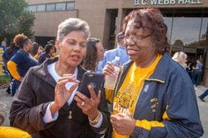 A woman showing something on her phone to another woman at a public event outside B.C. Webb Hall.