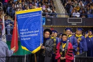 Graduates at a university commencement ceremony holding a College of Agriculture and Environmental S.