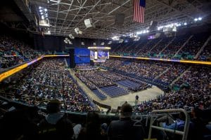 Graduation ceremony in a large indoor arena with a stage and audience.