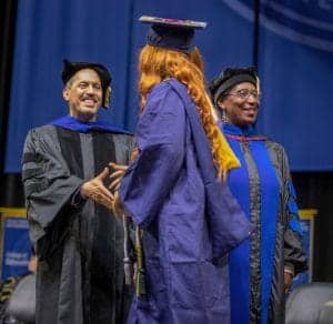 Graduation ceremony with faculty and graduate in academic regalia at CAES News event.