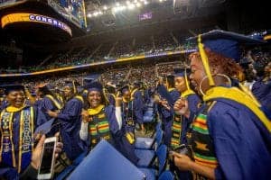 Graduates celebrating at a commencement ceremony in a large indoor stadium.