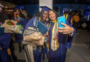 Graduates celebrating at a graduation ceremony, taking a selfie in caps and gowns.
