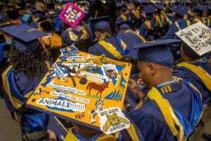 Graduation ceremony with students in caps and gowns holding a colorful poster celebrating achievemen.