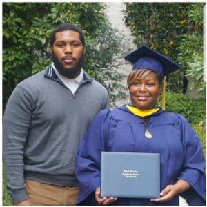 Graduation ceremony with graduate in cap and gown holding diploma outdoors.