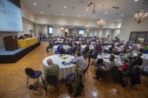High-capacity conference room with attendees listening to a speaker at a professional event.