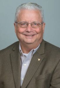 A senior man in a suit smiling, professional portrait for CAES News.
