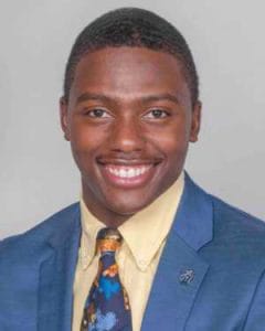 A young African American man in a blue suit smiling confidently.