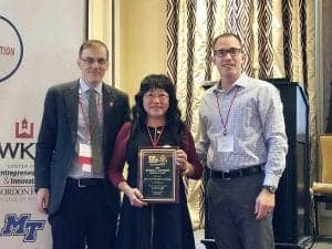 Celebration of achievement at CAES News event with three professionals holding an award plaque.