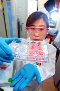 A scientist in a laboratory holding a tray of red and clear test tubes for scientific research.