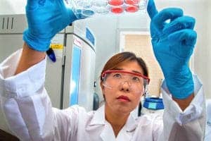 A scientist in a laboratory examining a test tube with a focused expression.