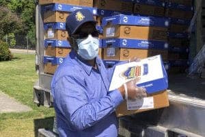 Delivery worker unloading boxes of supplies outdoors with a truck in background.