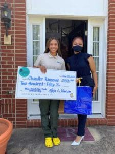 A woman and a girl holding a large check outside a house.