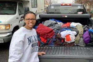 Clothing donation drive with a smiling woman standing next to a truck bed filled with clothes.