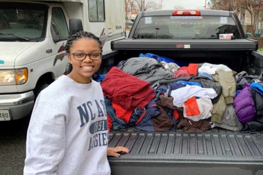 Clothing donation drive with a smiling woman standing next to a truck bed filled with clothes.