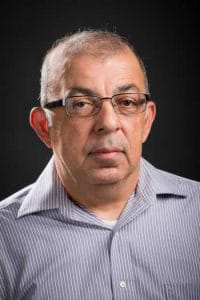 High-quality portrait of a middle-aged man with glasses, wearing a striped shirt, against a dark bac.