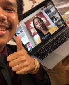 Person smiling and giving a thumbs-up during a video call on a laptop.