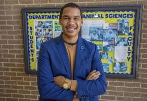 A student in a blue blazer standing in front of a Department of Animal Sciences bulletin board.