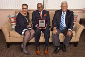Three professionals sitting on a sofa, holding an award plaque, smiling at the camera.
