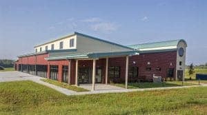 Modern educational facility with red brick and light blue roof in a green landscape.