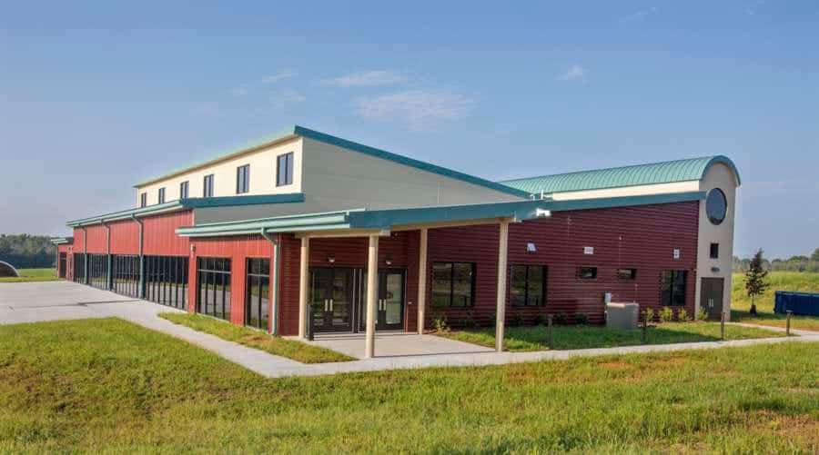 Modern educational facility with red brick and light blue roof in a green landscape.