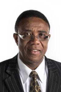 A man in a business suit with glasses, looking serious and professional.